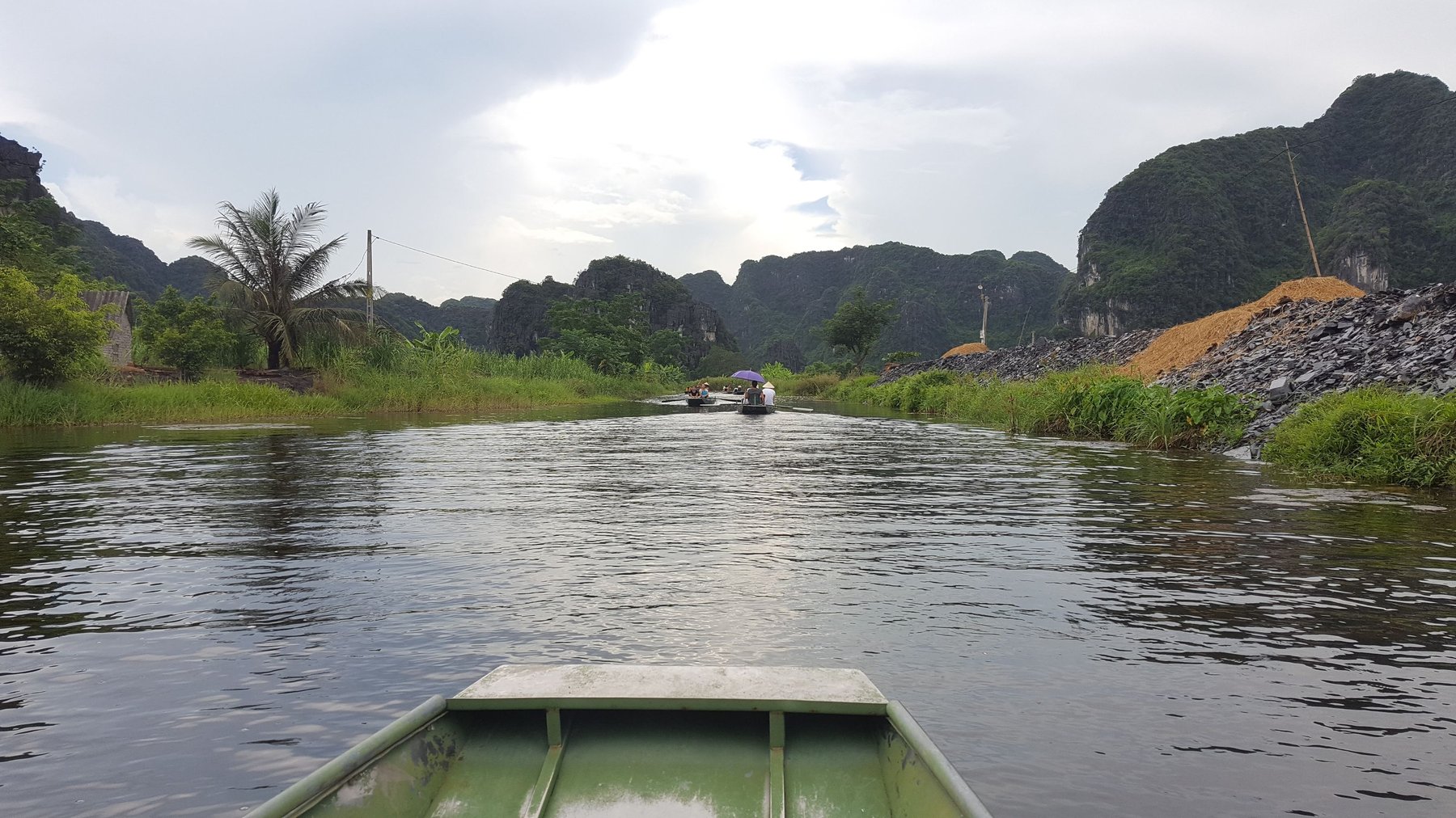 A calm river with mountains in the distance, and small green rowboats.