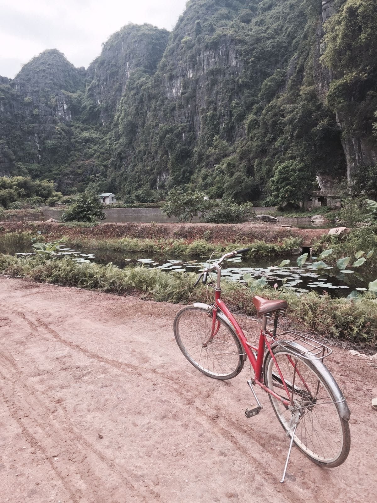 A red bicycle propped up on a dirt road in front of a mountain.