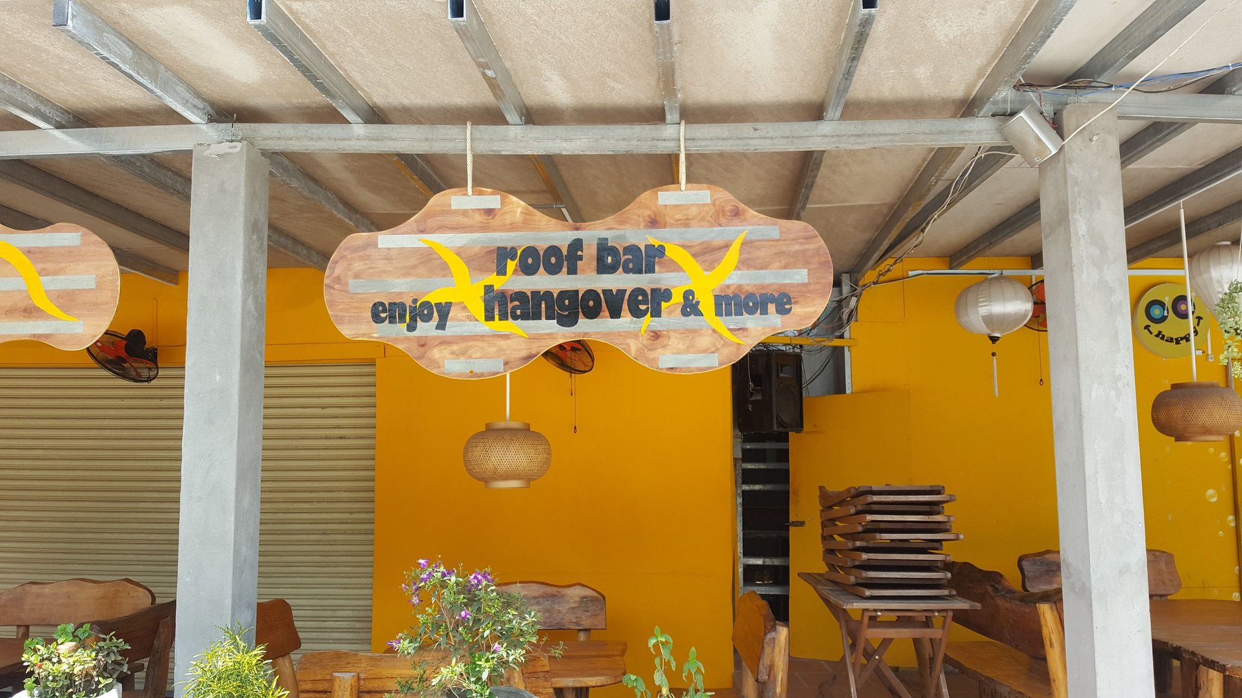 A wooden sign in front of a bar reads “roof bar - enjoy hangover & more”.