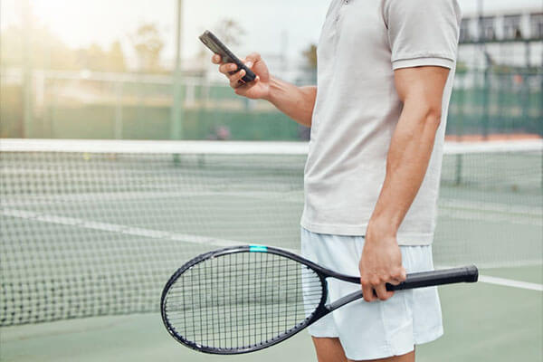Tennis player on a court with a smartphone and racket, representing the use of apps to improve tennis skills.