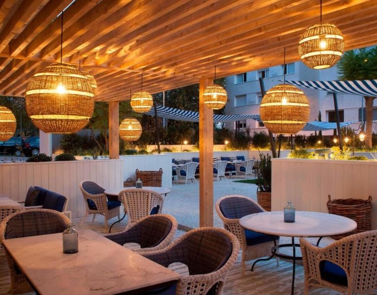 Outdoor dining area at AC Hotels with wicker furniture, marble tables, and ambient hanging lamps.