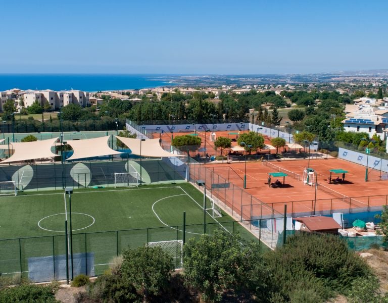 Aerial view of Aphrodite Hills sports complex featuring padel courts and football pitches with the Mediterranean Sea in the background.