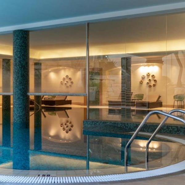 Indoor pool at Aphrodite Hills Resort with modern design, ambient lighting, and glass walls.