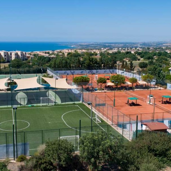 Panoramic view of Aphrodite Hills tennis courts in Cyprus, featuring artificial turf and clay courts with the Mediterranean Sea in the background.