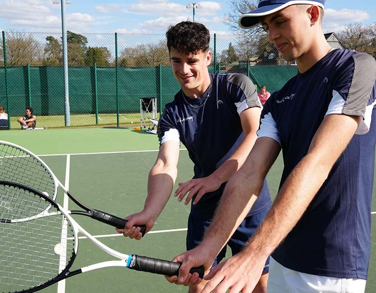 Two young male tennis players in navy sportswear holding rackets at Active Away Junior Tennis Camp, Royal Russell School tennis court.