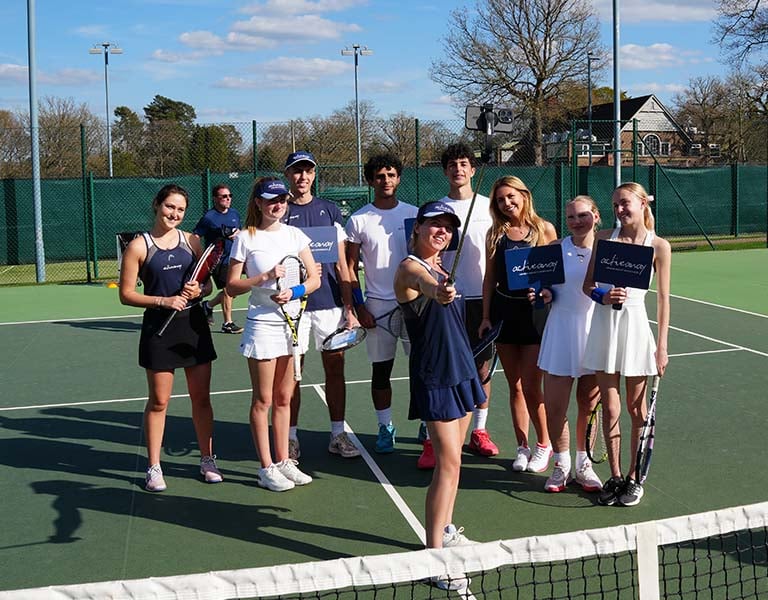 Group of junior tennis players smiling on an outdoor court at Royal Russell School during Active Away Tennis Camps.