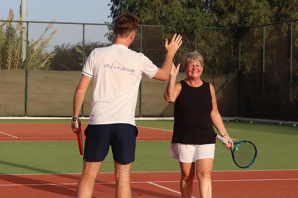 Man and woman high-fiving on a tennis court, showcasing camaraderie during an Active Away tennis event.