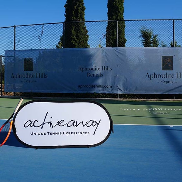Tennis court at Aphrodite Hills Resort in Cyprus with an Active Away Unique Tennis Experiences banner.