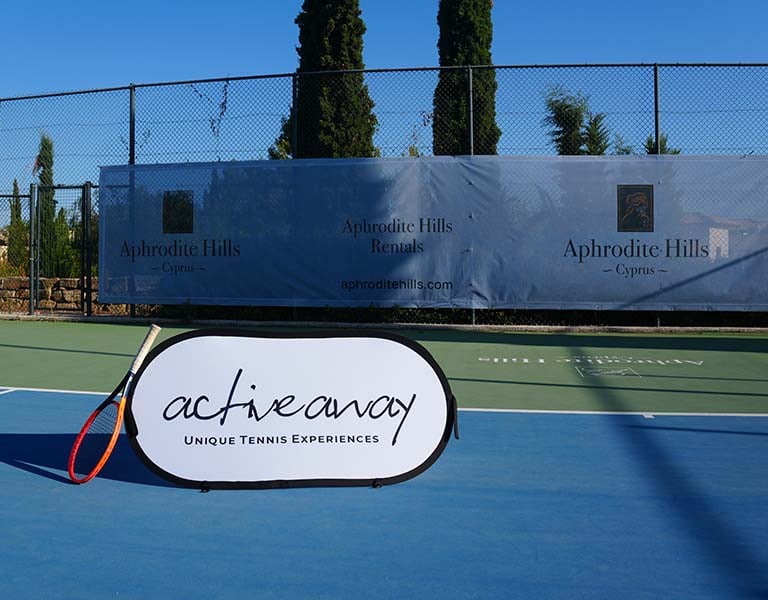 Tennis court at Aphrodite Hills Resort in Cyprus with an Active Away Unique Tennis Experiences banner.