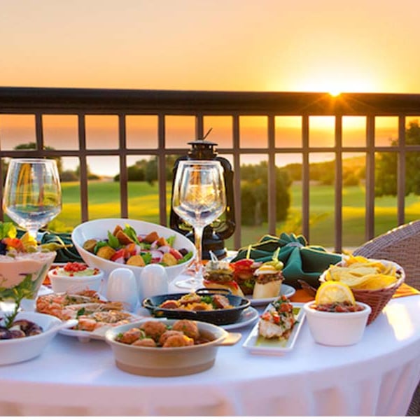 Gourmet dining setup with appetisers and wine on a table overlooking a sunset at Aphrodite Hills Resort.