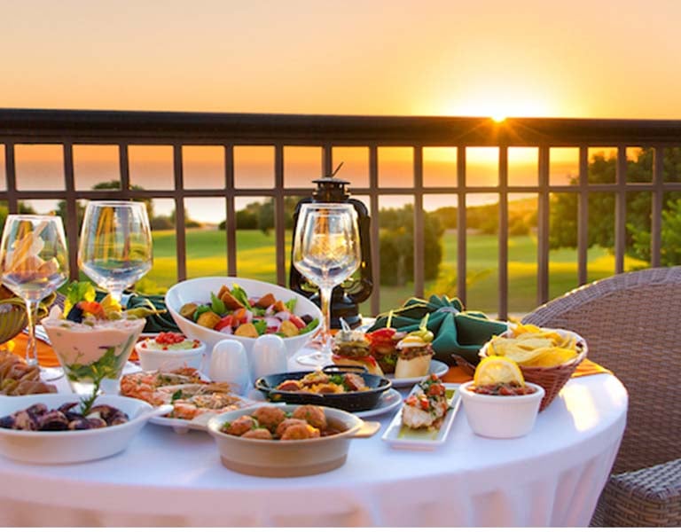 Gourmet dining setup with appetisers and wine on a table overlooking a sunset at Aphrodite Hills Resort.