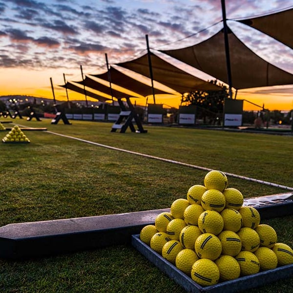 Sunset view of Aphrodite Hills driving range with stacks of yellow golf balls and canopy shades.
