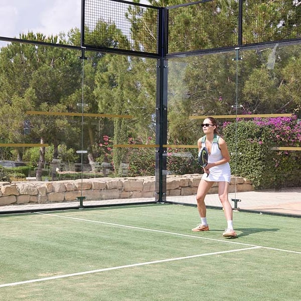 Woman playing padel tennis at Aphrodite Hills Resort, Cyprus, standing on the court with a racket and ready to receive a serve.