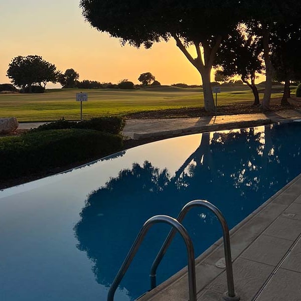 Infinity pool at Aphrodite Hills Resort with sunset reflection and view of golf course.