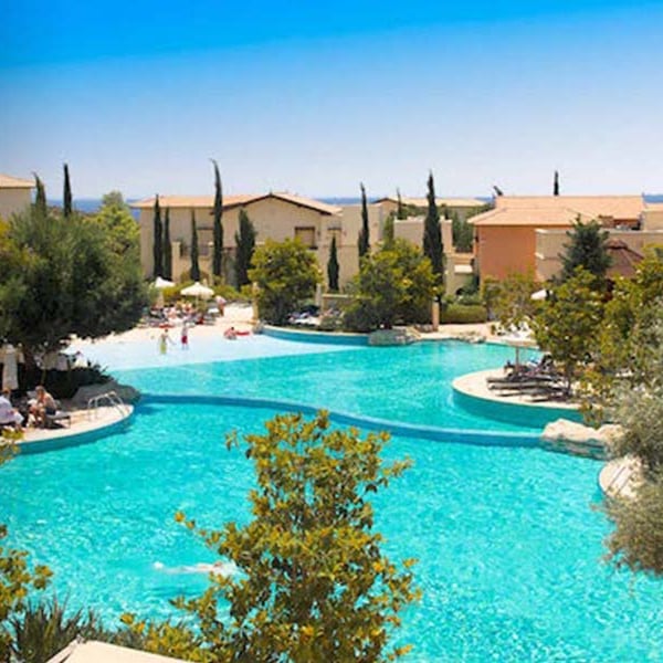 Luxurious pools at Aphrodite Hills resort surrounded by greenery and Mediterranean buildings.