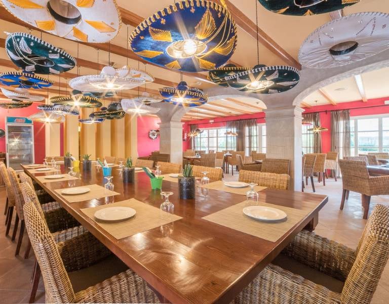 Restaurant at Beach Club Family Holiday with a long dining table, wicker chairs, and sombrero ceiling decorations.