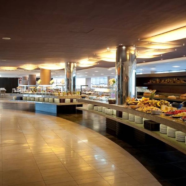 Luxurious beach club buffet with curved counters and an assortment of fruits, pastries, and gourmet dishes under ambient lighting.