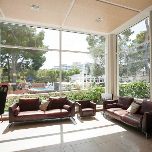 Beach club lobby with leather sofas and large windows overlooking an outdoor pool area and greenery.