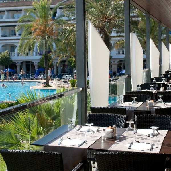 Outdoor dining area at a beach club restaurant with tables overlooking a pool and palm trees.