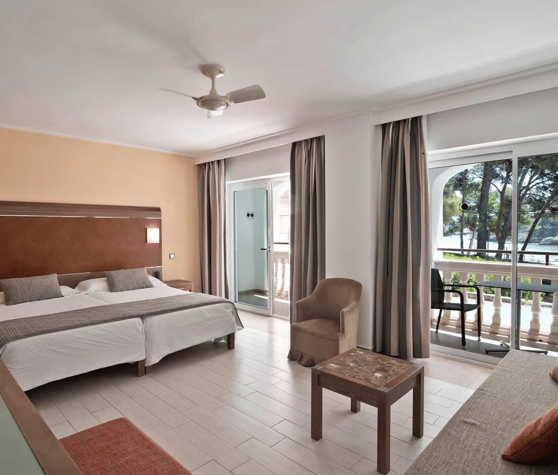 Beach club standard room with two single beds, a balcony showing a sea view, an armchair, and neutral decor.