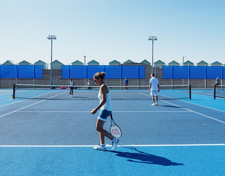 Players on a blue padel court at Brighton Tennis Padel, engaging in a doubles match on a sunny day.