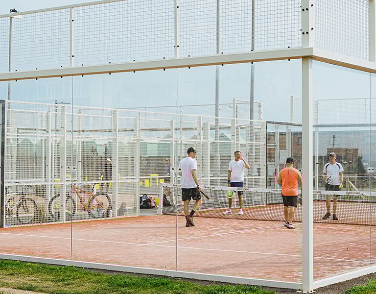Players playing doubles padel tennis on an outdoor glass-walled court in Brighton.