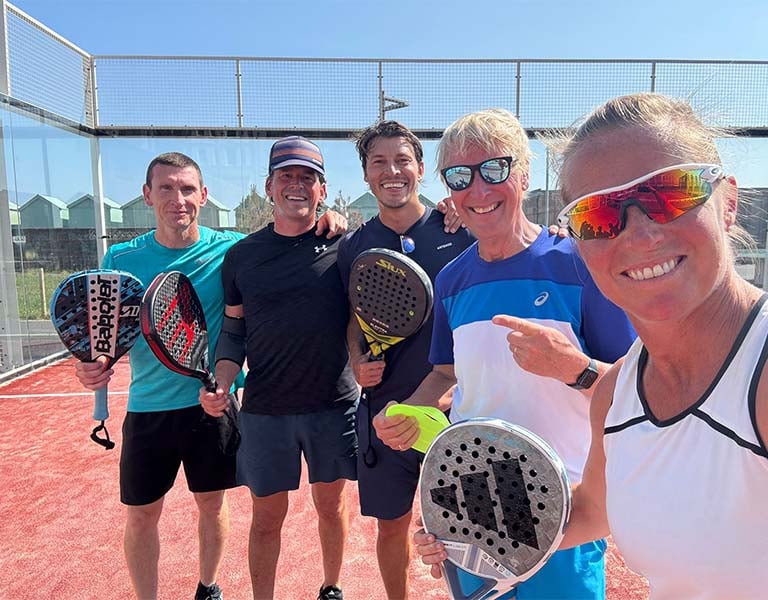 Five people standing on a red padel court, each holding a padel racket, on a sunny day in Brighton.