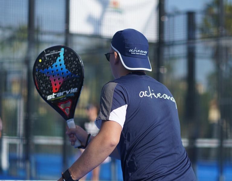 Padel coach holding a StarVie racket on an outdoor court with a blue activewear uniform.