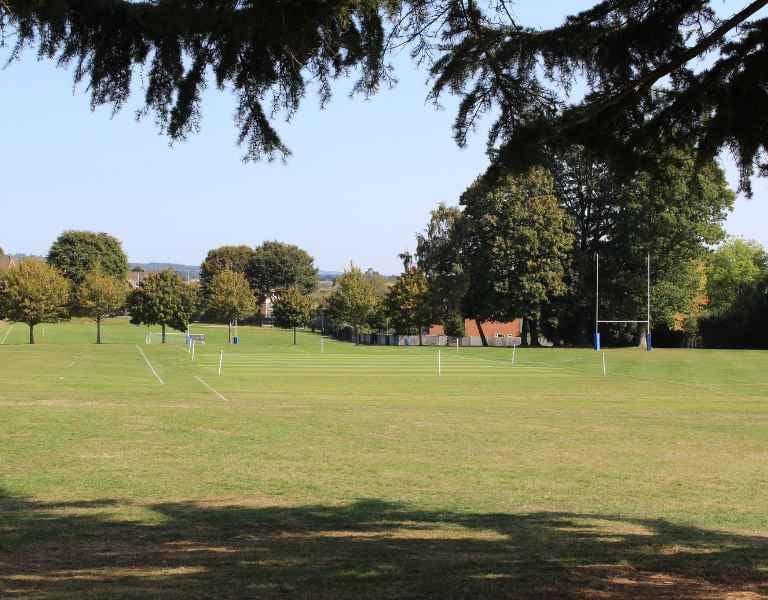 Churcher's School outdoor grass courts on a sunny day, with rugby posts and sports field markings surrounded by trees.