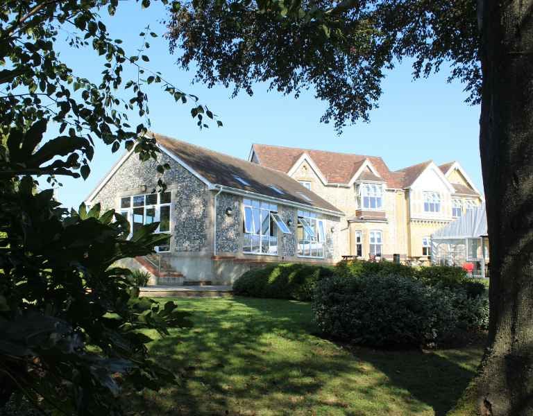 Outdoor view of Churcher's School student dormitories with traditional stone and brick architecture surrounded by greenery.