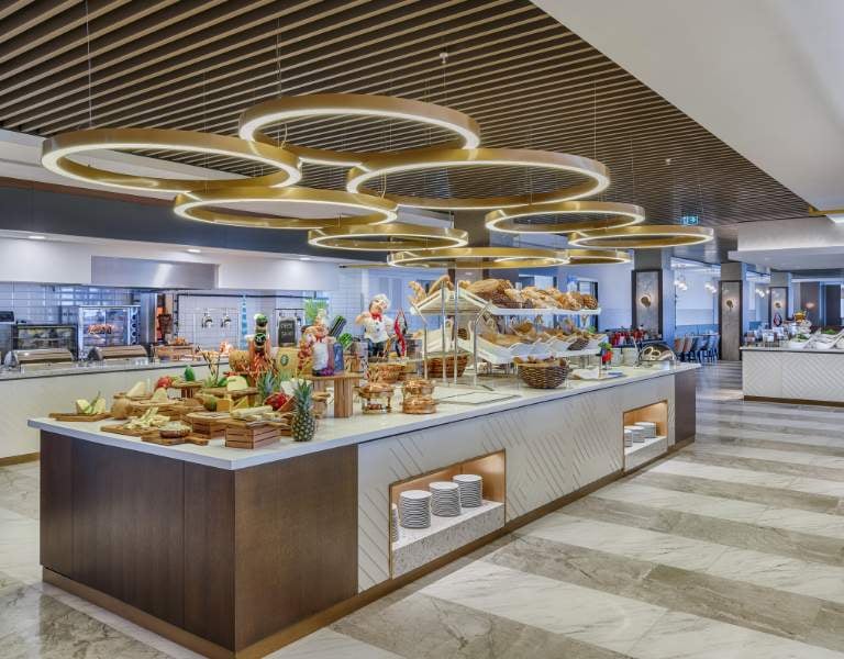Buffet area in a modern dining space with various food items, stylish lighting, and a contemporary design at Corendon.