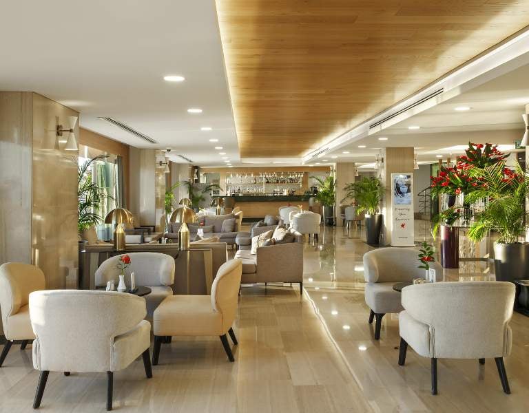Spacious lounge with modern beige armchairs, wooden ceiling, and indoor plants at Corendon Gallery.