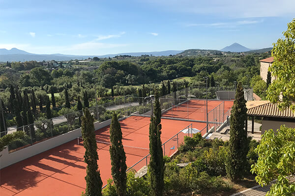 Elevated view of tennis courts at Costa Navarino, surrounded by cypress trees and the Peloponnese mountains in the background.