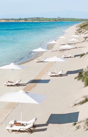 Beach with white sun loungers and umbrellas along the sandy shore facing the clear blue sea.