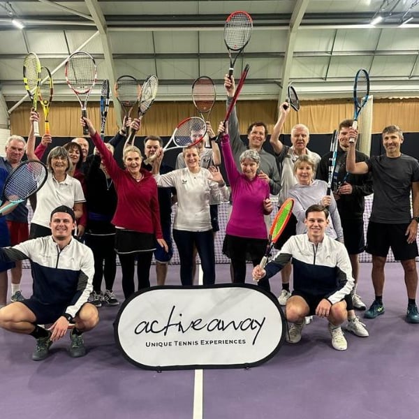 Group of tennis players at DL Bristol Gallery holding up racquets, participating in an Active Away event on an indoor court.