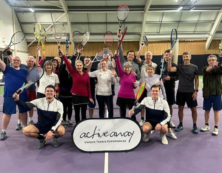 Group of tennis players at DL Bristol Gallery holding up racquets, participating in an Active Away event on an indoor court.