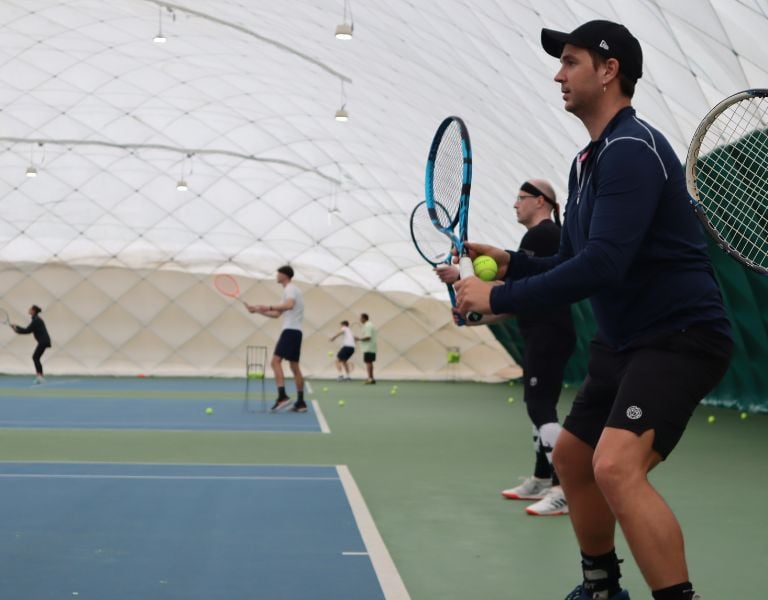 Tennis players and a coach at an indoor court during an Active Away session in Beaconsfield, poised to play.