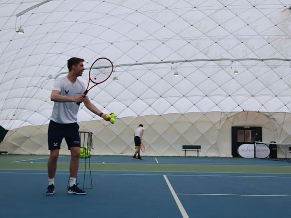 Tennis coaches on court under a dome, feeding tennis balls, with Active Away logo visible, indoors at Beaconsfield.