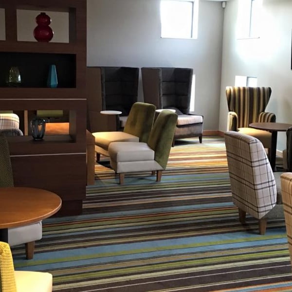 Modern club room with assorted armchairs, sofas, decorative shelving with vases, a flat-screen television, and striped carpet.