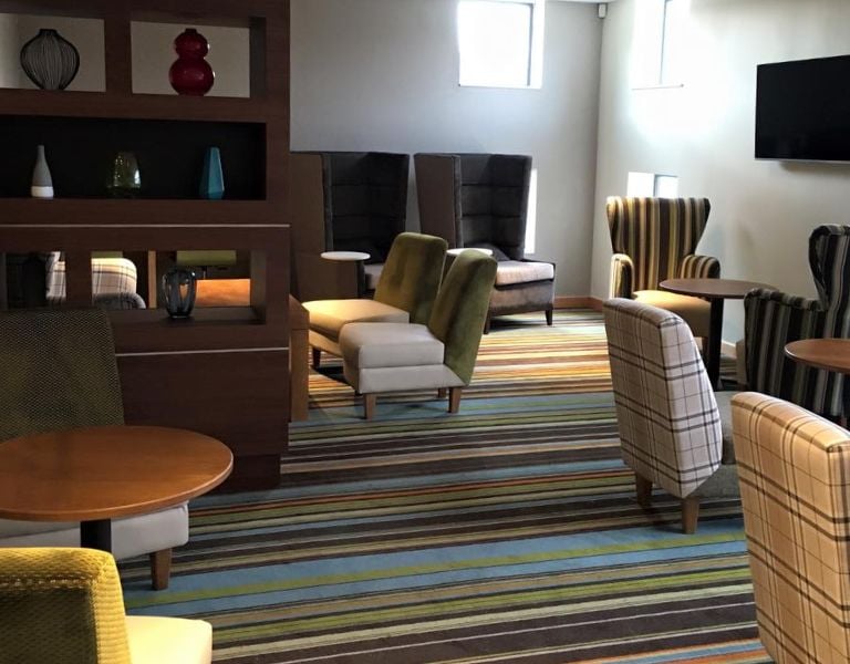 Modern club room with assorted armchairs, sofas, decorative shelving with vases, a flat-screen television, and striped carpet.