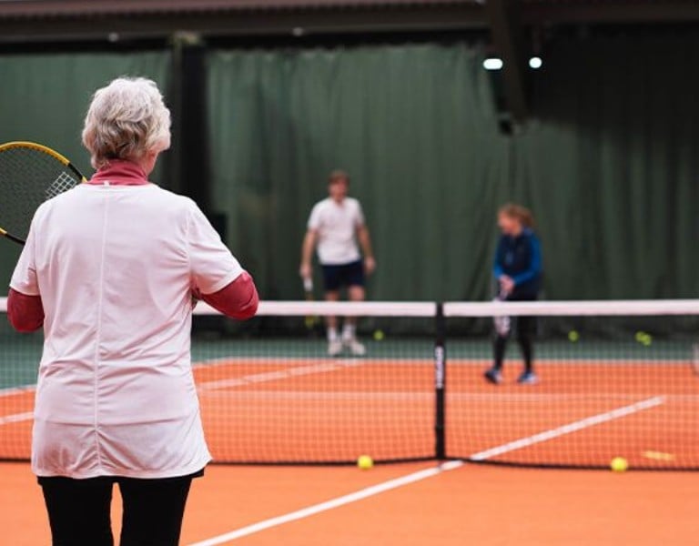 Indoor tennis lesson at DL Cheshire Oaks with a coach observing a young player on court.