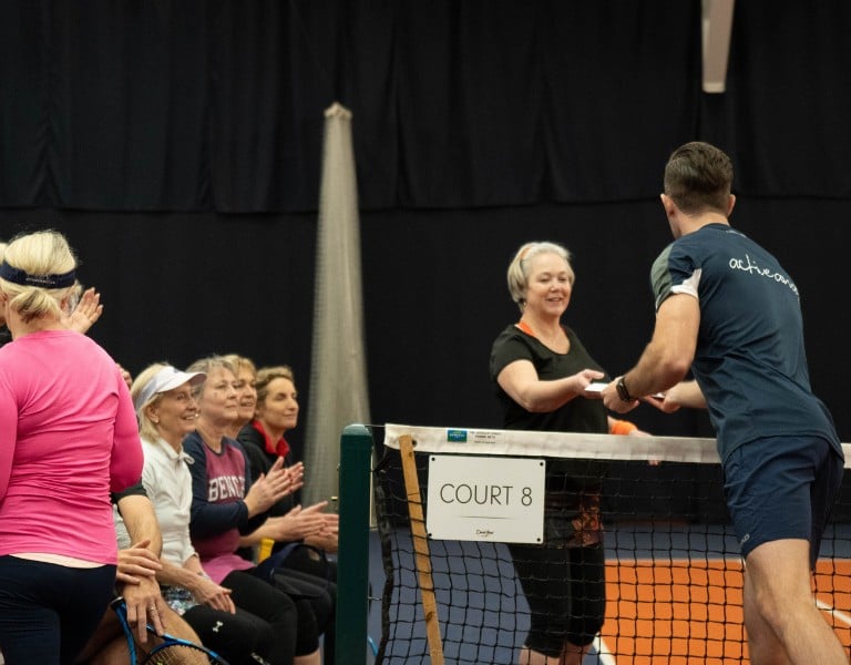 Tennis coach distributing refreshments to female players on a bench at Cheshire Oaks.