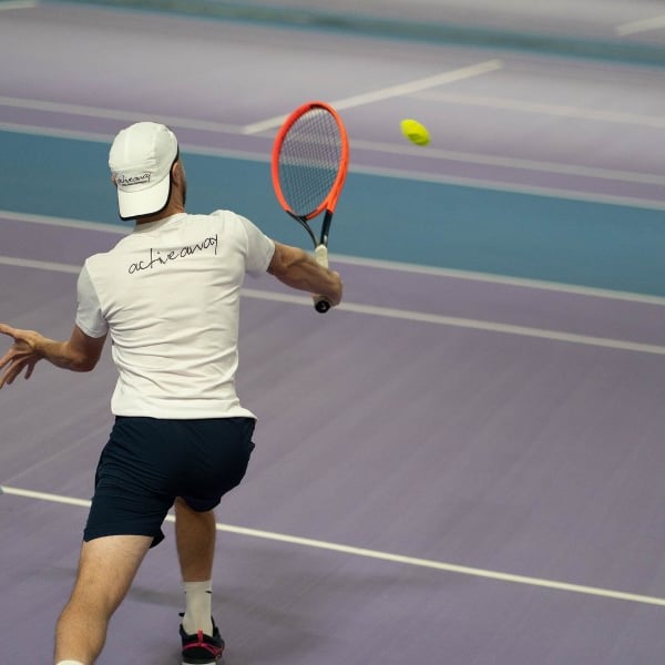 Tennis coach hitting a backhand shot with an orange racquet on indoor courts at DL Chorley.