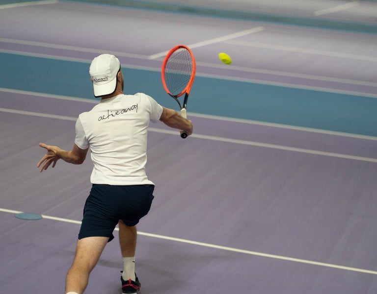 Tennis coach hitting a backhand shot with an orange racquet on indoor courts at DL Chorley.