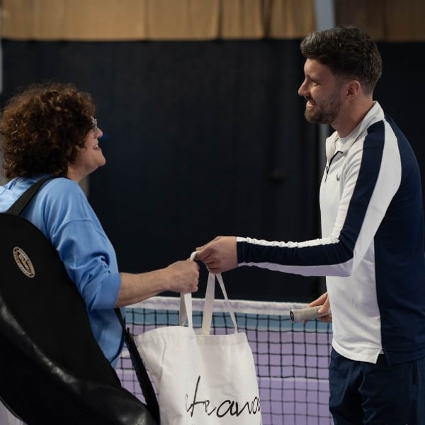 Man and woman on an indoor tennis court at DL Chorley Gallery, engaging in a friendly exchange with tennis gear in hand.