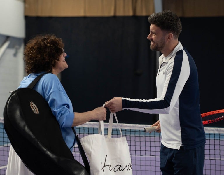 Man and woman on an indoor tennis court at DL Chorley Gallery, engaging in a friendly exchange with tennis gear in hand.