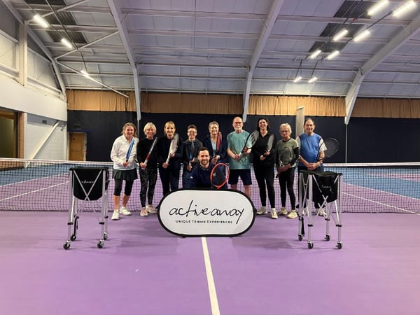 Group photo of participants at the Active Away tennis break in Edinburgh, standing on a purple indoor court holding tennis rackets and a banner.