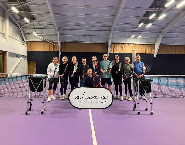 Group photo of participants at the Active Away tennis break in Edinburgh, standing on a purple indoor court holding tennis rackets and a banner.