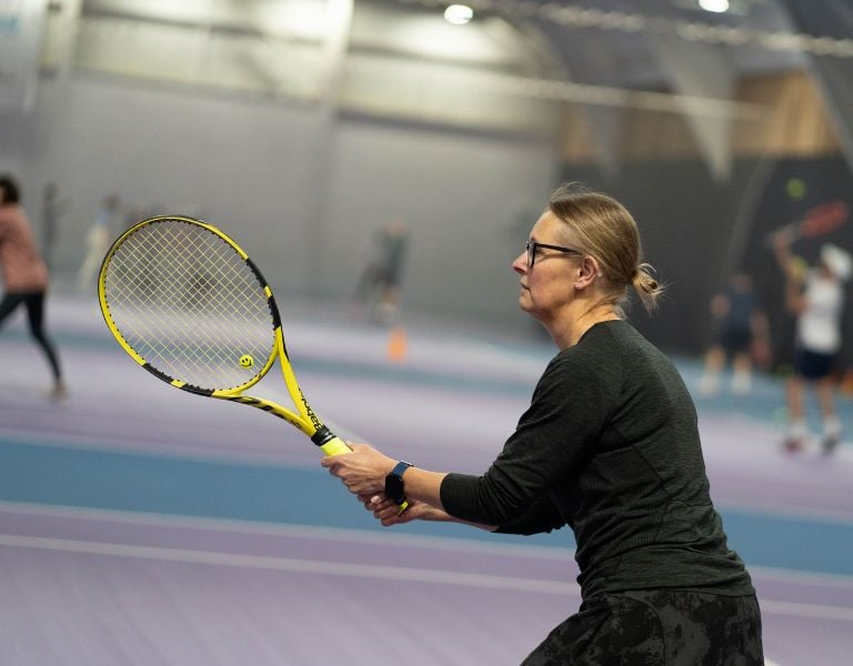 Female tennis player holding a yellow racket, preparing to return a shot at DL Edinburgh's indoor tennis court.
