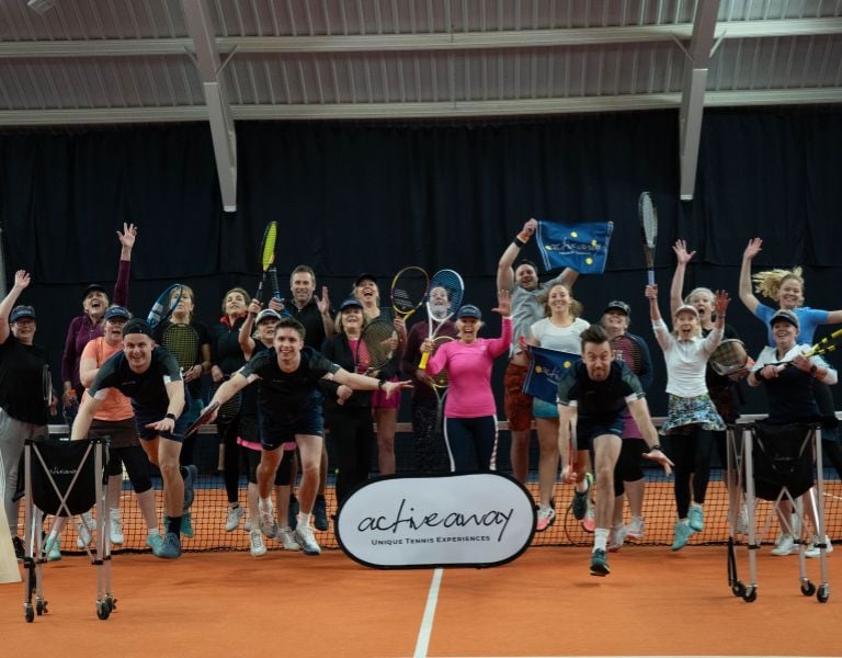 A group of excited tennis players jumping with rackets on an indoor court, promoting Active Away's unique tennis experiences.